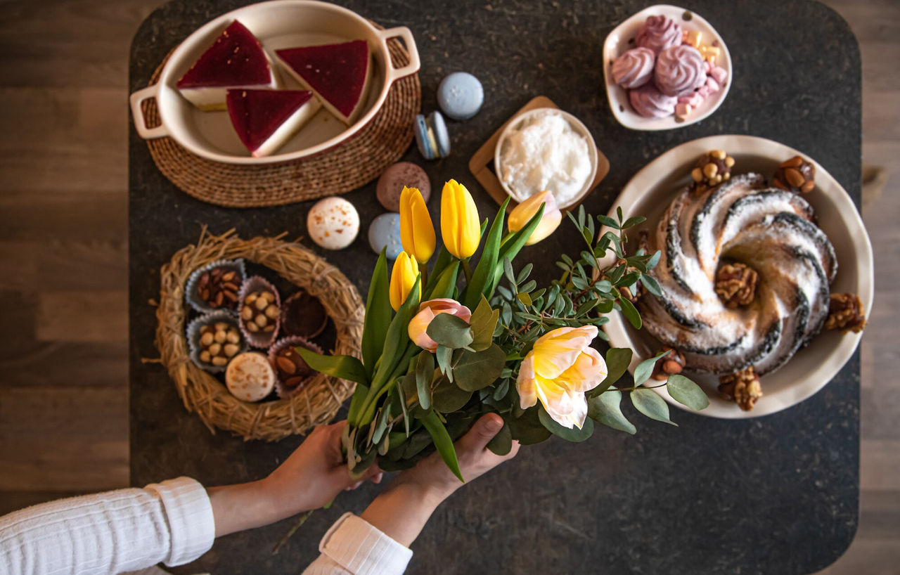 Bovenaanzicht van een desserttafel met diverse gebakjes, snoepjes en een boeket verse tulpen.