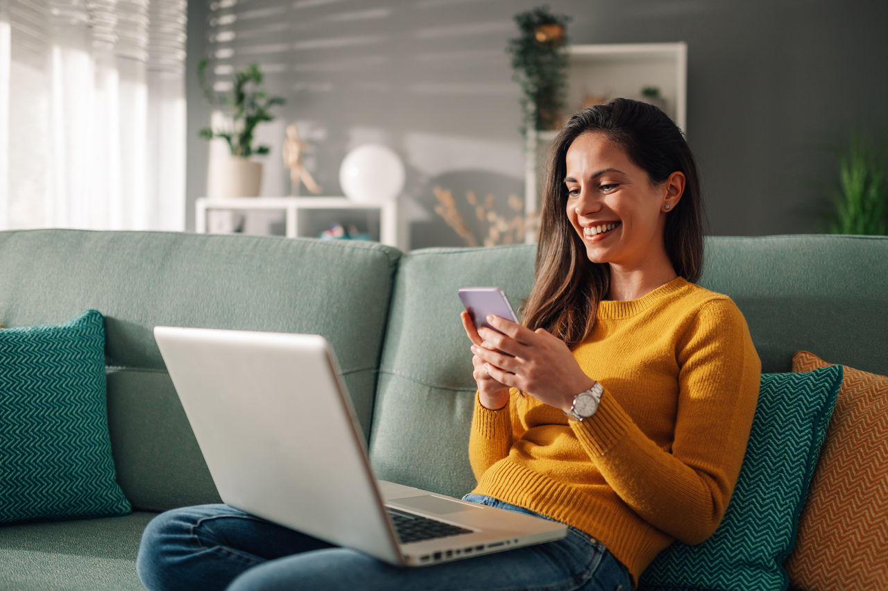 Vrouw multitasking met een laptop en smartphone.