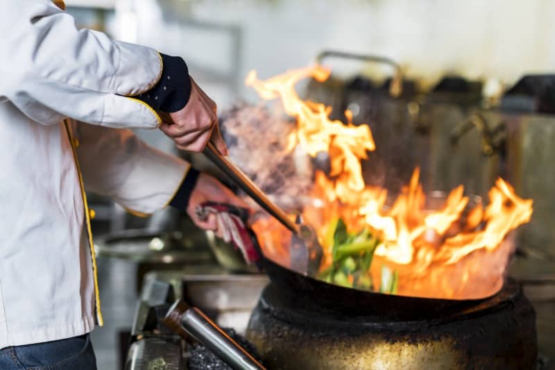 Chef stirring food in wok over flames