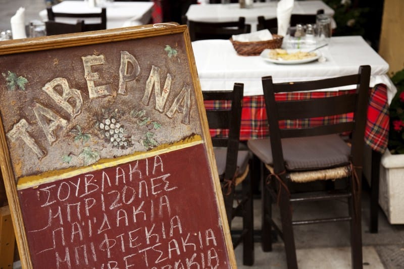 Sidewalk sign in front of tables outside Greek restaurant