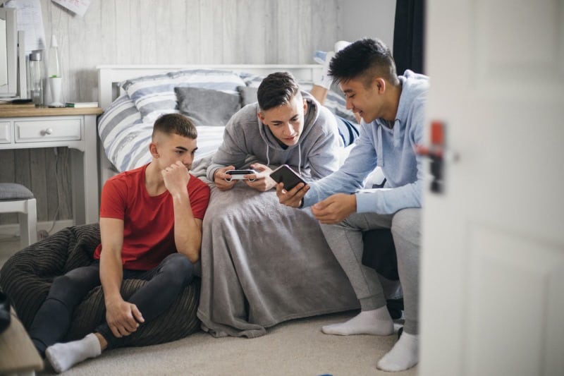 3 teenage male friends hanging out in their room looking at phones