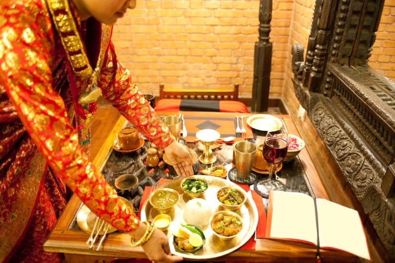 Waitress in Indian restaurant setting down platter of food on table