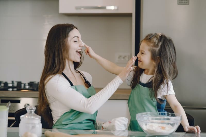 Mom and daughter being silly putting flour ron each other's nose in a kitchen